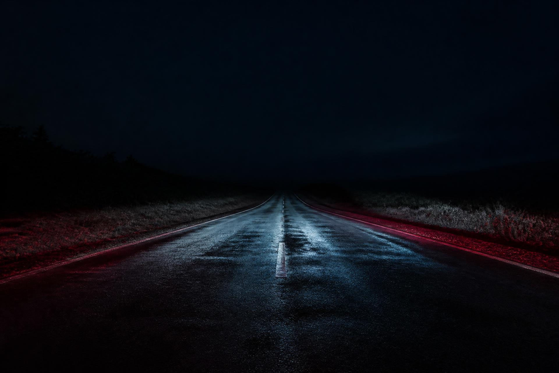 Empty asphalt road at night lit by a faint red glow